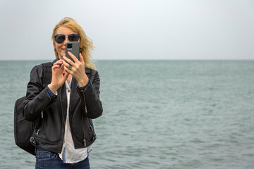 An adult woman in a black jacket and with a backpack on her shoulders takes photos on her...