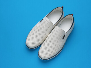 Pair of White Slip-On Loafers on Bright Blue Background - Modern Minimalist Footwear Concept