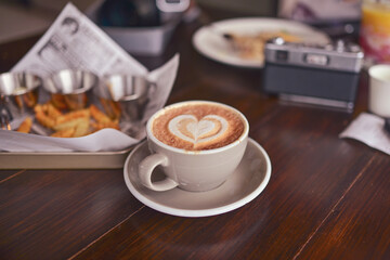 Coffee in a heart-shaped cup on a table with a camera and snacks on a plate