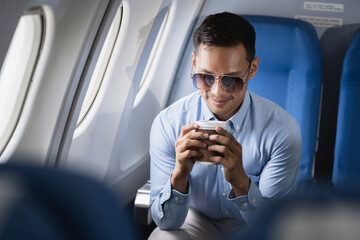 Asian man enjoying enjoys a coffee comfortable flight while sitting in the airplane cabin,...