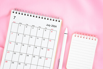July 2024 month calendar and pen with open diary on pink fabric background.