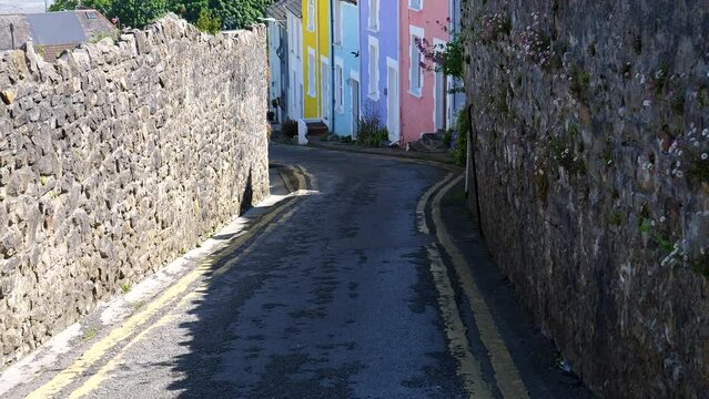 Tilt up shot showing colourful street houses in Mumbles, crow flying toward camera, looking downhill towards Swansea Bay beach.