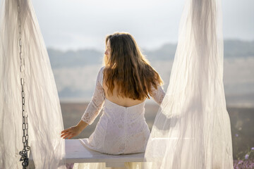 A woman in a white dress sits on a bench under a white canopy. The scene is serene and peaceful,...