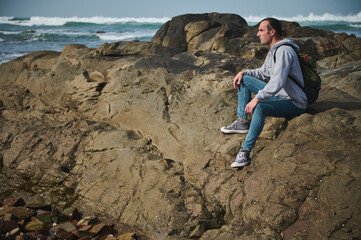 Man hiking along rocky coastline with ocean waves in the background