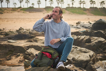 Smiling man talking on phone while sitting on rocks at a beach
