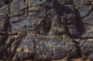  Close-up of a natural rock formation showcasing rugged textures and detailed weathering patterns. The rocky surface displays layers and cracks, indicating the effects of natural erosion.