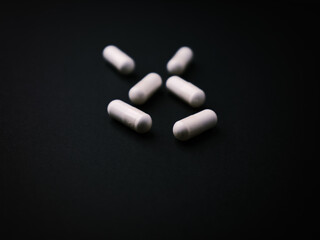 Creatine capsules on dark paper background. Soft focus. Close up. Copy space.	