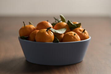 Small organic tangerines with leaves in ceramic bowl on wood table