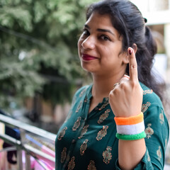 Smart young lady showing her ink-marked fingers after casting votes in front of polling booth of...