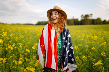 Beautiful young woman holding an American flag in the wind in a field. Patriotic holiday. USA...