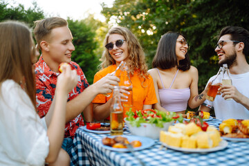 Group of young happy friends having picnic outdoors. People having fun and celebrating while grilling ata barbacue party. Vacation, picnic, weekend, nature