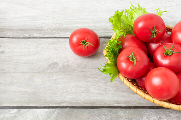 Ripe tomatoes in a basket with lettuce leaves on a light wooden background