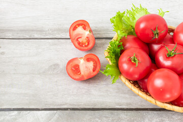 Ripe tomatoes in a basket with lettuce leaves on a light wooden background