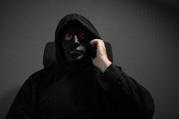Money swindler, a man in a mask talking on the phone, committing online theft of digital currency.