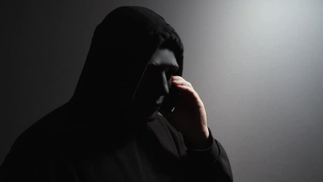 A man in a mask talking on the phone, criminal plotting fraud, anonymous hacker preparing cyber attack, burglar coordinating theft.