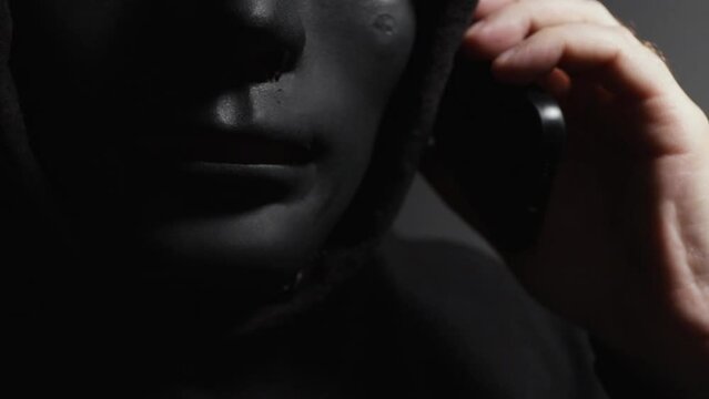 Money swindler, a man in a mask talking on the phone, cyber crime involving stolen banking information.
