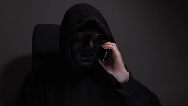 Phone Scammers, man in a mask with a phone, fake messages for bank fraud, cyber crime and security threat, identity and privacy attack.