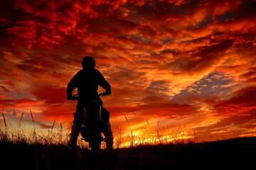Fototapeta premium A motocross rider's silhouette against a fiery sunset sky