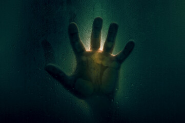 Horror scene of a man against wet glass. Hand against the background of a wet glass bathroom wall....