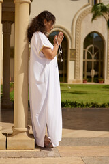 Woman praying outdoors with prayer beads in a serene setting
