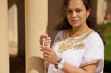 Woman holding prayer beads in a serene outdoor setting, spiritual and contemplative moment