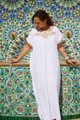 Woman in white traditional dress against a colorful Moroccan mosaic background