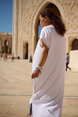 Woman in traditional white attire with prayer beads in front of an ornate mosque entrance