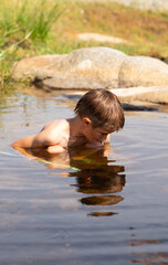 Fototapeta premium Boy bathing in a river looking into something