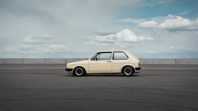 Side profile view of classic Volkswagen Golf hatchback. Beige Volkswagen Golf mk1 stationary on big empty parking lot with cloudy sky in the background. Kyiv, Ukraine - April 18 2015.