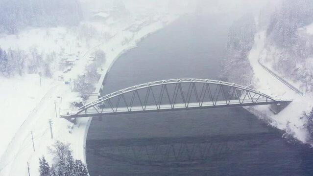 4K Aerial view landscape of Meta bridge over the river between the mountain and small town in snow day. 