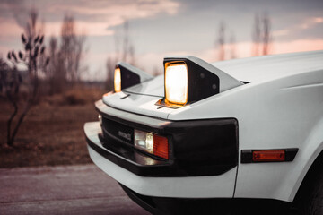 White old japanese 1980s car with pop-up headlights. Blurry countryside in the background