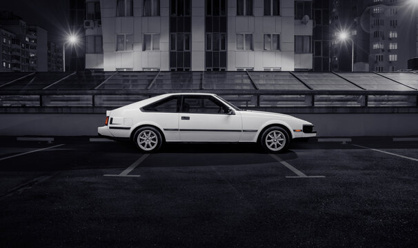 white Toyota Celica Supra liftback coupe parked on city street. Side profile view of sporty japanese 1980s car in front of night urban background. Kyiv, Ukraine - March 01 2015.