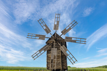 Old rustic windmill on the rye field under the blue sky with clouds. Gorgeous summer rural scenery.