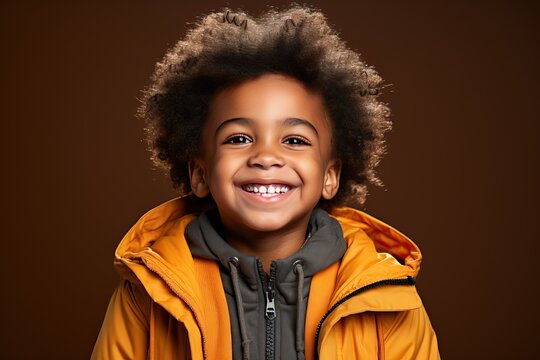 Portrait of a little afro boy with afro curls in a yellow jacket on a red background.