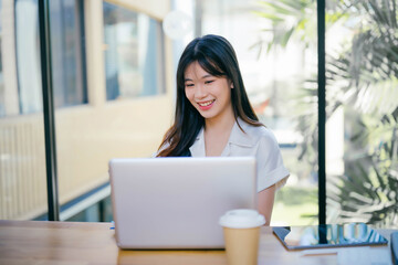 Young Professional Woman Working on Laptop in Modern Office with Natural Light and Greenery in the Background