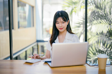 Young Professional Woman Working on Laptop in Modern Office with Natural Light and Greenery in the Background