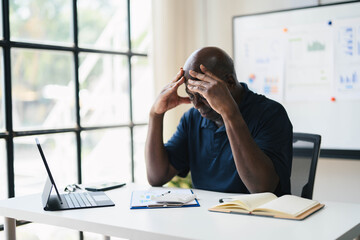Naklejka premium Stressed Businessman at Desk with Laptop and Documents in Modern Office Setting, Analyzing Data and Financial Reports, Experiencing Work Pressure and Fatigue