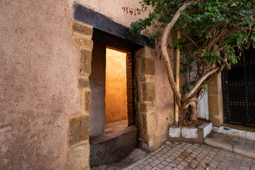 view of the entrance to an alley illuminated by the sun and the warm colors of the walls. A large...