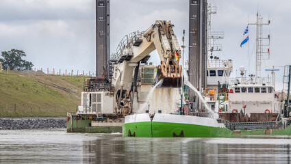 Bagger am Nord-Ostseekanal mit großer Schaufel aus der Wasser strömt