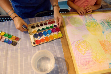 Children enjoying art class with teacher, painting with watercolors in a creative workshop