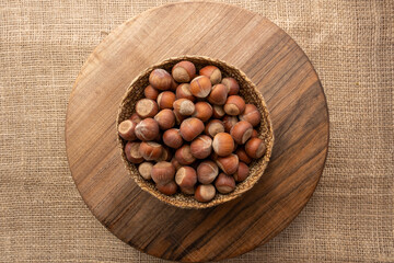Overhead view of a wicker bowl full of shelled hazelnuts on a wooden surface