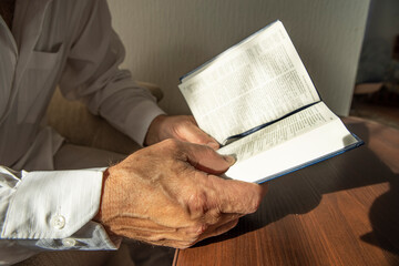 Hands of senior man holding Holy Bible at home. Lifestyle, natural aesthetic light.