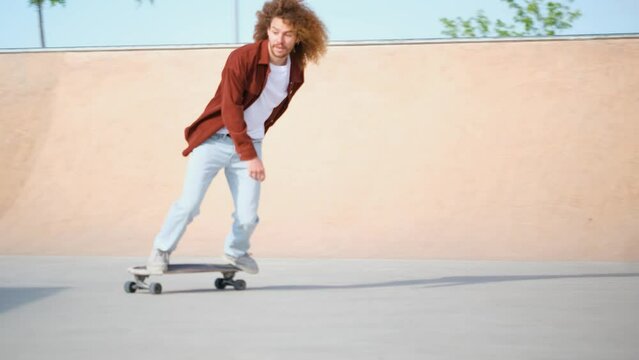 Latin young man with curly hair is skateboarding, riding down a ramp in a skate park.