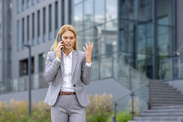 Businesswoman in a suit expressing frustration while talking on the phone outside an office...