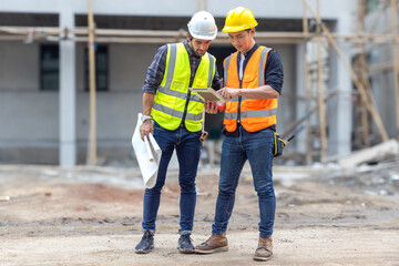 Foreman, engineer or architect with safety helmet holding laptop and blueprints for inspection details on construction in a new real estate construction site with crane and mechanical equipments.