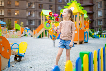 a child girl on the playground in the courtyard of a multi-storey house in the summer has fun...