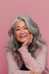 Naklejka premium A woman with grey hair smiles in front of a pink background