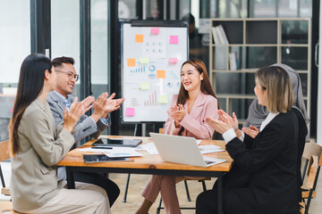 Diverse business team applauding and celebrating success during a meeting, with charts and graphs on the board.