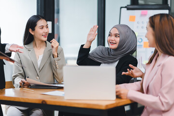 Cheerful business team actively engaging and sharing ideas during an office meeting, using documents and a laptop.
