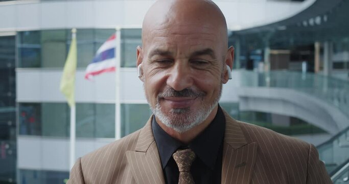 Attractive man with bald head and goatee in stylish suit and wireless headphones gives infectious smile. Positive attitude and friendly look at ease. Sincere smile emphasizes confidence and openness.